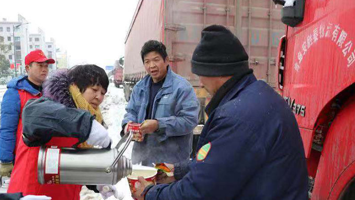 【一城冰雪一城暖】热水、面包、牛奶……看到街道旁边的马路上有大量货车因冰雪天气滞留,长龙街道的党员干部和志愿者们为司机送上吃的喝的,社区搭建了临时的爱心驿站,为他们提供免费的食物和温暖的落脚点。<br><br>为了让滞留的司机平安度过冰雪天气,长界社区的“新时代讲习所”变成了临时的爱心驿站,驿站内暖风阵阵,食物充足,还有热水供应。“怎么样?很丰盛吧?”傍晚,在社区“爱心驿站”内谈笑声阵阵,戚师傅领到热气腾腾的盒饭后,迫不及待地拨通家人的视频报平安,还不忘“炫耀”自己丰盛的晚餐。<br><br>“我们还专门誊出了一间房间,让他们晚上休息。”长界社区书记郭俏告诉记者,社区还贴心地在各个路口设置了指引牌指引路过滞留的司机前往“爱心驿站”避寒取暖。<br>目前,还有十几位司机在爱心驿站休息。<br>